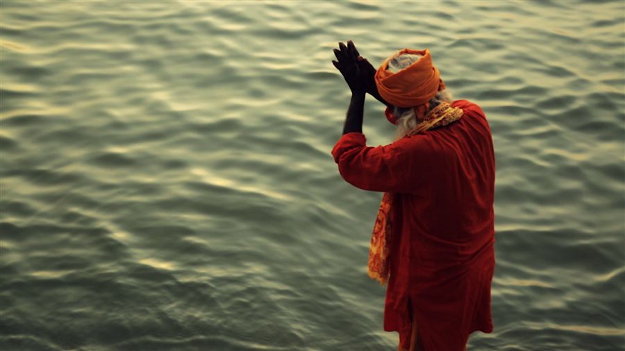 A sadhu in saffron praying at the river's edge